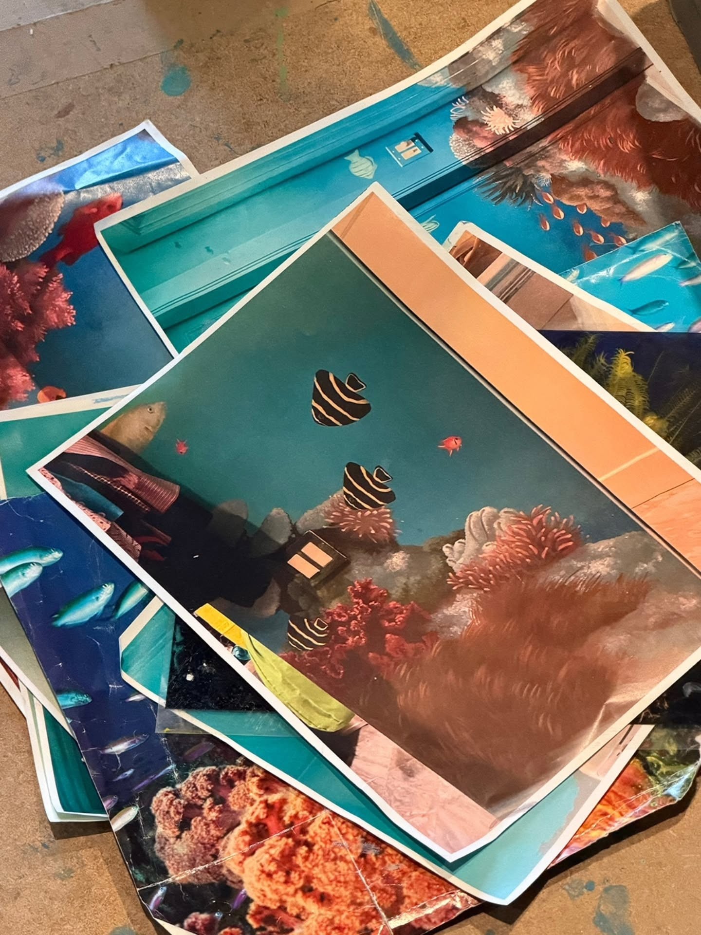 Reference prints and source imagery spread on the studio floor during design and layout phase